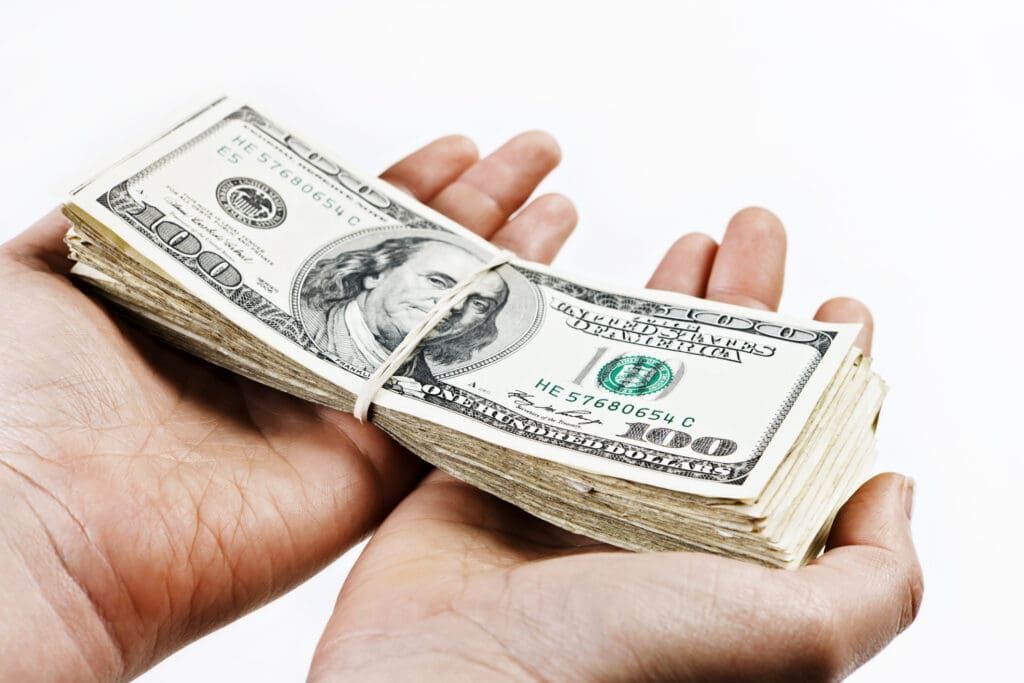A pair of hands holds out a large bundle of US dollars. Isolated on white.